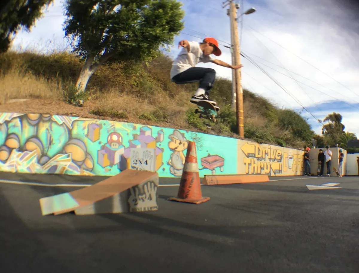 Child ollieing off the end of one foot high by two foot wide launch ramp over a safety cone